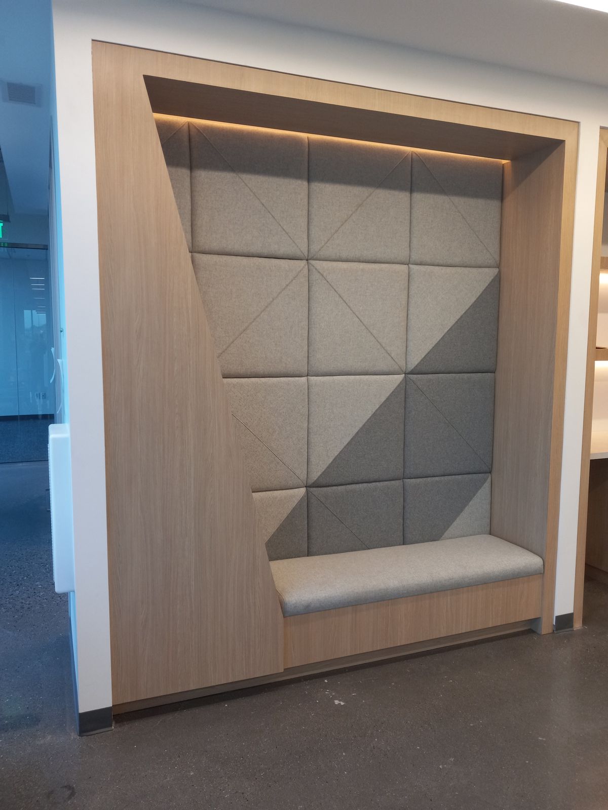 Custom oak-framed wall niche with tufted gray panels and upholstered bench seat
